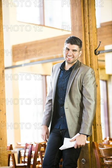 Caucasian man leaning on beam in cafe holding paperwork