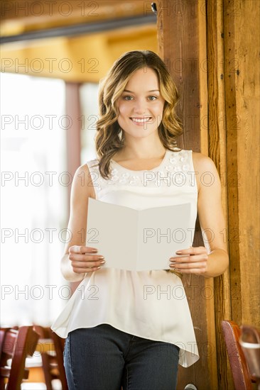 Caucasian woman leaning on beam in cafe holding menu