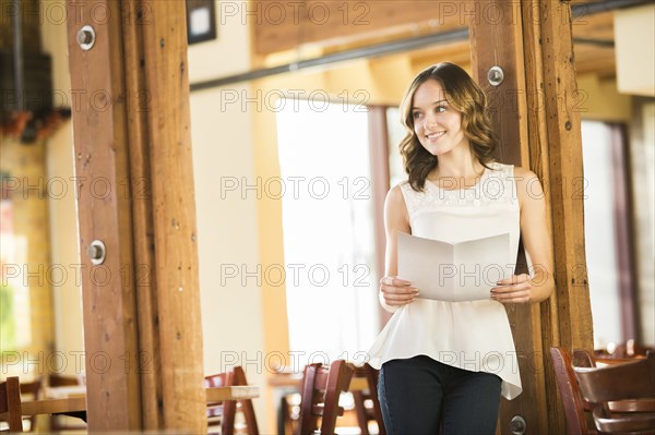 Caucasian woman leaning on beam in cafe holding menu