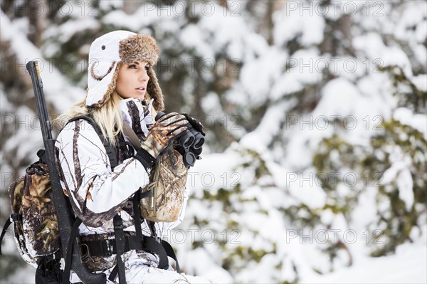 Caucasian woman hunting in forest with binoculars