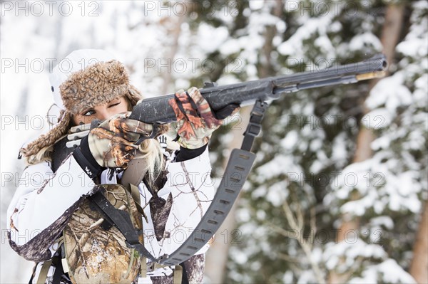 Caucasian woman hunting in forest aiming rifle