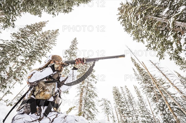 Caucasian woman hunting in forest aiming rifle