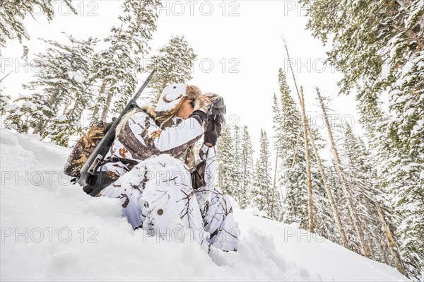 Caucasian woman hunting in forest using binoculars