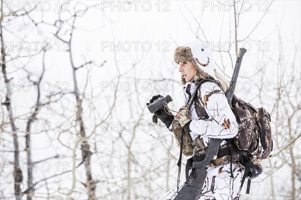 Caucasian woman hunting in forest using binoculars