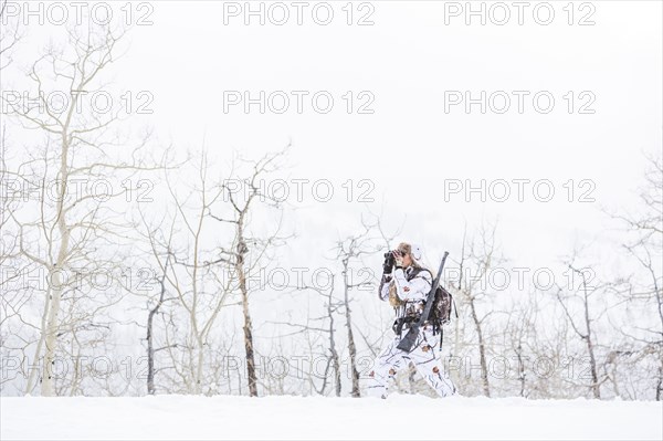 Caucasian woman hunting in forest using binoculars