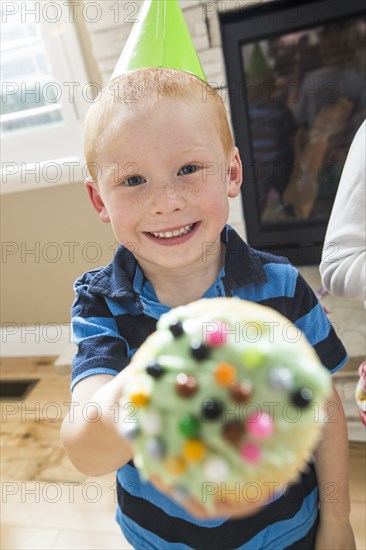 Caucasian boy wearing party hat showing cupcake