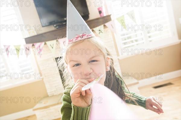 Caucasian girl wearing party hat blowing party horn blower