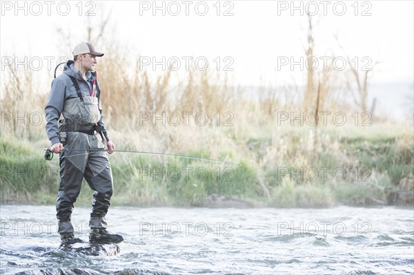 Caucasian man fly fishing on rock in river