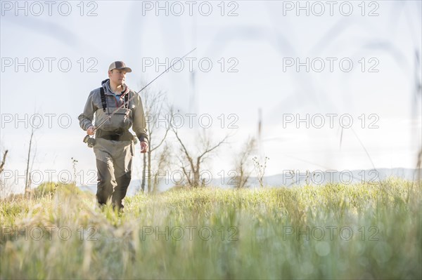 Caucasian man carrying fishing rod in field