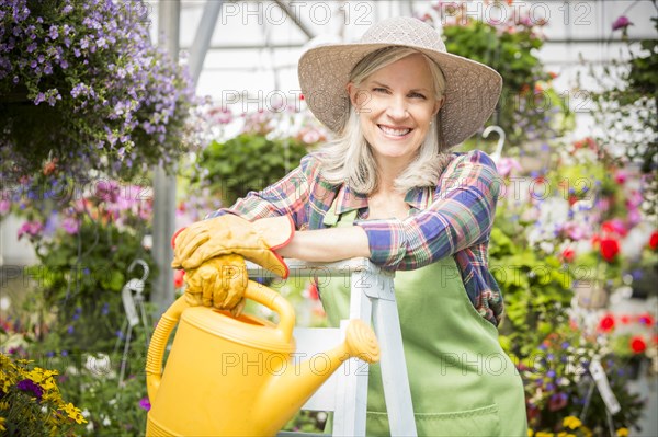 Caucasian woman holding watering can on ladder in greenhouse