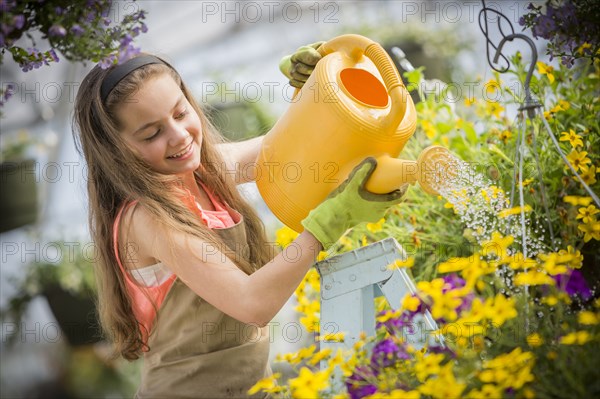 Caucasian girl on ladder watering flowers in greenhouse