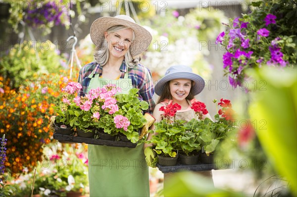 Caucasian grandmother and granddaughter holding potted plants in greenhouse