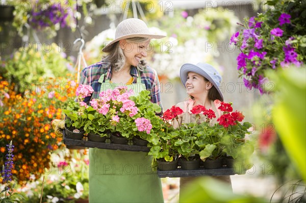 Caucasian grandmother and granddaughter holding potted plants in greenhouse