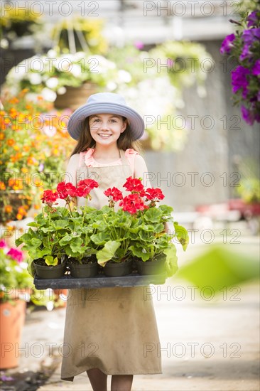 Caucasian girl holding potted plants in greenhouse
