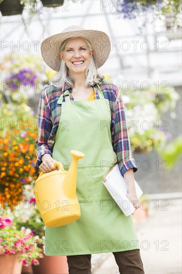 Caucasian woman holding clipboard and watering can in greenhouse