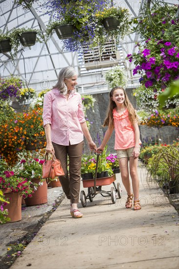 Caucasian grandmother and granddaughter pulling cart in greenhouse