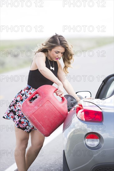 Caucasian woman pouring fuel from gas can into sports car