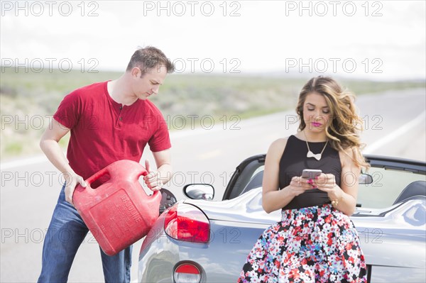 Caucasian man pouring fuel from gas can into sports car