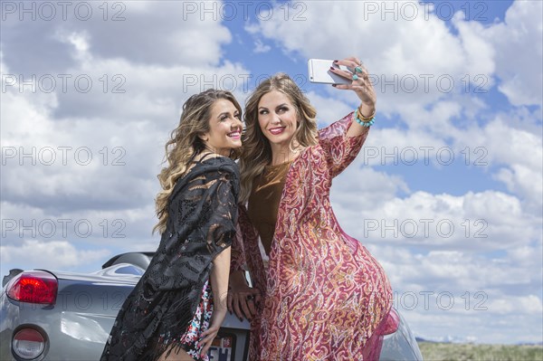 Caucasian women taking cell phone selfie at sports car