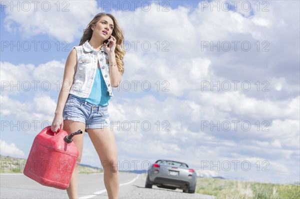 Caucasian woman holding gas can talking on cell phone