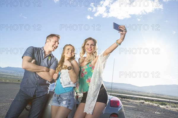 Caucasian friends posing for cell phone selfie at sports car