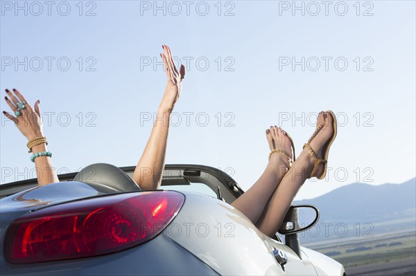 Caucasian woman with arms raised and feet up in sports car