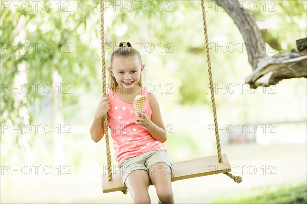 Caucasian girl eating ice cream cone on rope swing