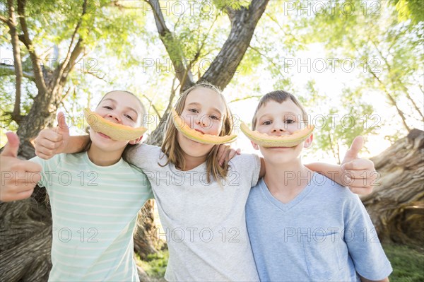Caucasian boy and girls smiling with cantaloupe rinds