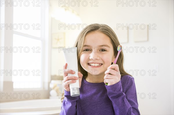 Smiling Caucasian girl holding toothbrush and toothpaste tube in bathroom