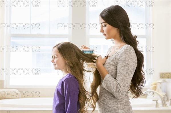 Mother brushing hair of daughter in bathroom