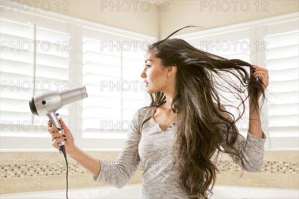 Mixed Race woman drying hair in bathroom