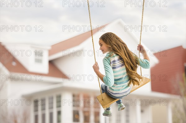 Caucasian girl on rope swing near house