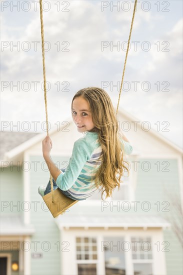 Caucasian girl on rope swing near house