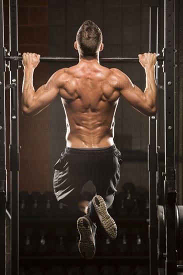 Caucasian man doing chin-up in gymnasium