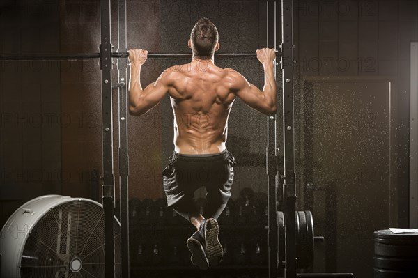 Caucasian man doing chin-up in gymnasium