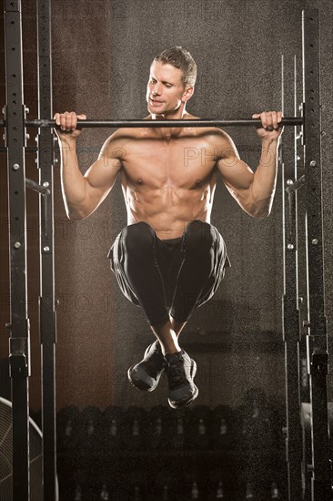 Caucasian man doing chin-up in gymnasium