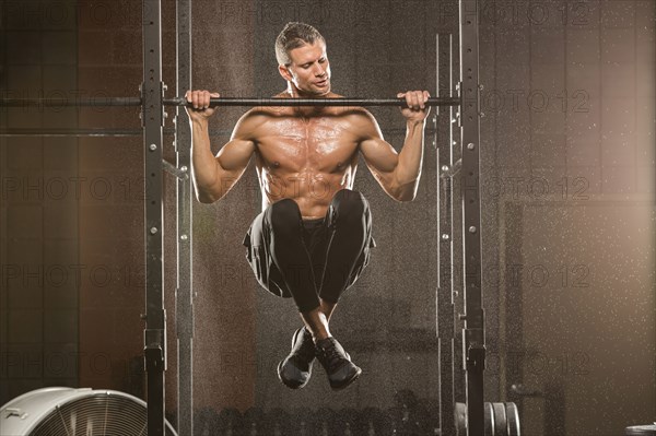 Caucasian man doing chin-up in gymnasium