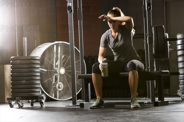 Caucasian woman wiping forehead on bench in gymnasium