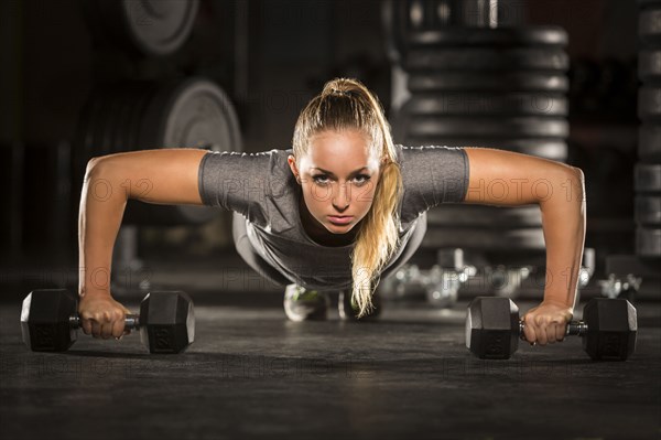 Caucasian woman doing push-up using dumbbells in gymnasium