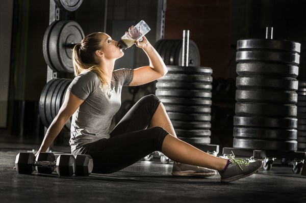 Caucasian woman drinking juice on floor in gymnasium