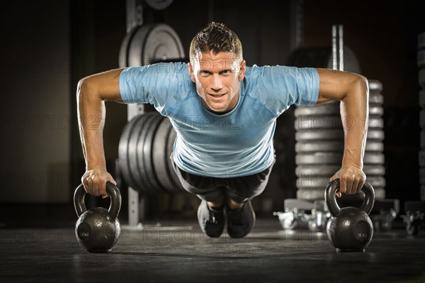 Caucasian man doing push-up using kettlebells in gymnasium