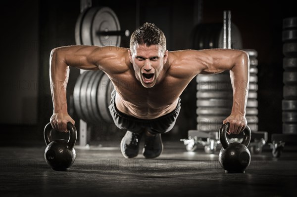 Caucasian man doing push-up using kettlebells in gymnasium