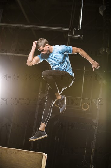 Caucasian man jumping on box in gymnasium