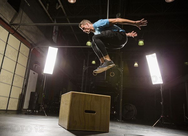 Caucasian man jumping on box in gymnasium