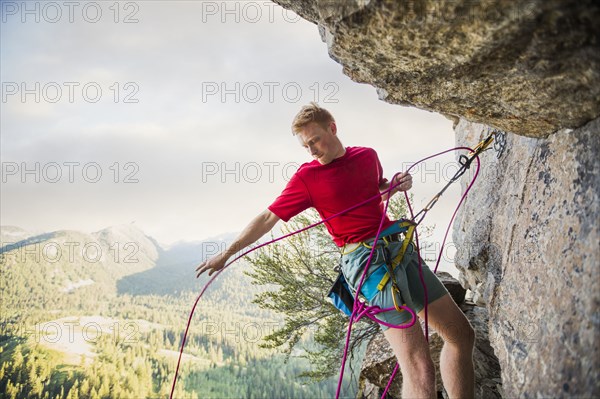 Caucasian man adjusting rope while rock climbing