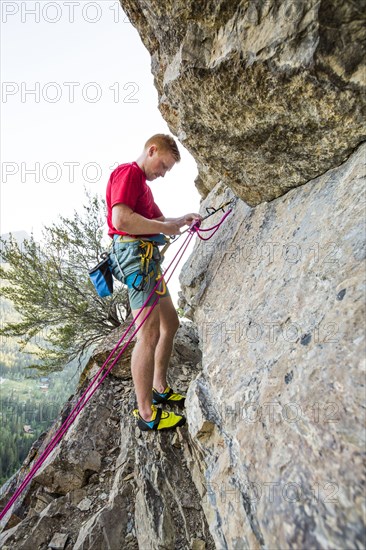 Caucasian man adjusting rope while rock climbing