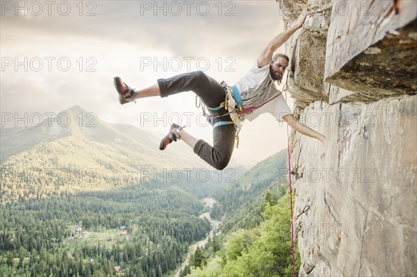 Caucasian man hanging from rock while climbing