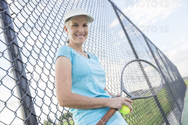 Caucasian woman holding tennis racket leaning on fence