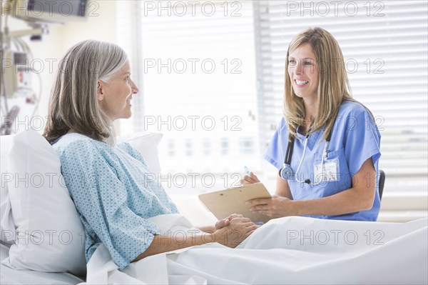 Caucasian nurse talking with woman in hospital bed