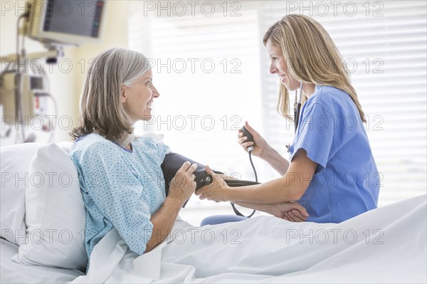 Caucasian nurse measuring blood pressure of woman in hospital bed